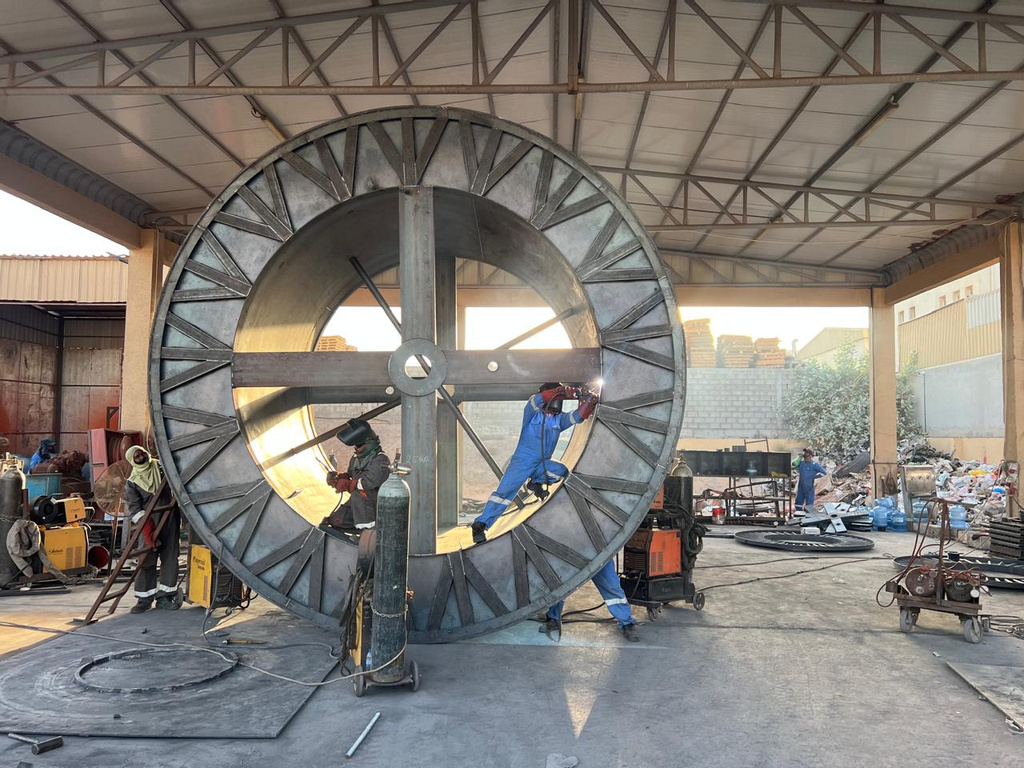 Technicians welding a large steel cable drum inside the workshop